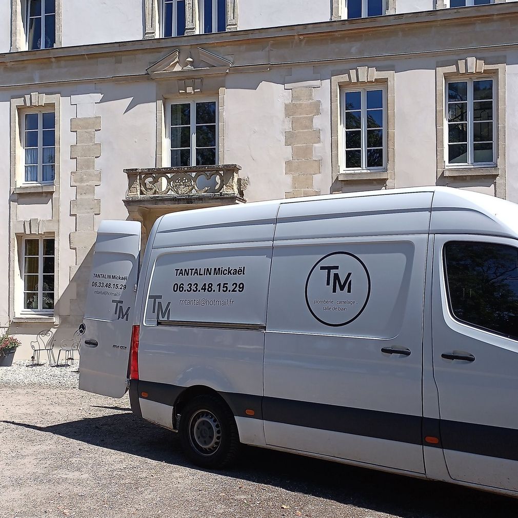 Une camionnette est garée devant un bâtiment en pierre avec une enseigne commerciale imprimée sur le côté.