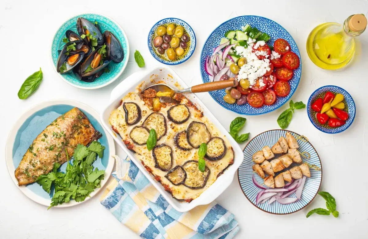 Fotografía cenital de varios platos griegos: musaca, ensalada, pescado a la parrilla, mejillones