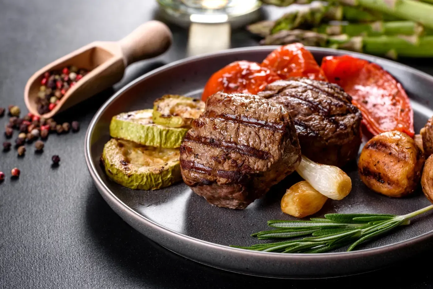 Medallones de bistec a la parrilla con verduras asadas en un plato gris.