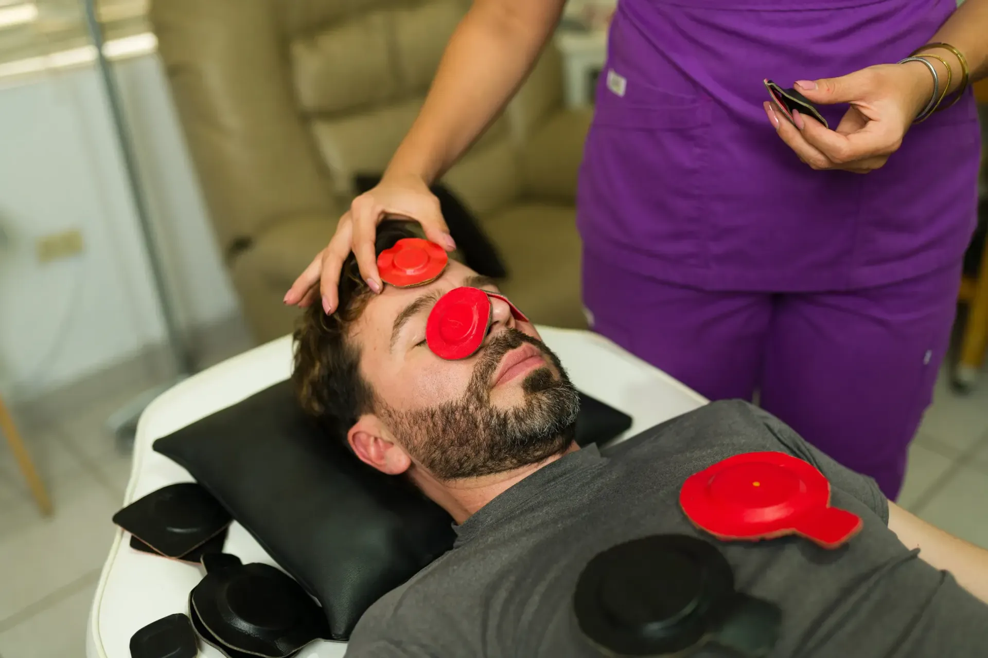 Hombre recibe fototerapia con dispositivos rojos y negros en el rostro y el pecho.