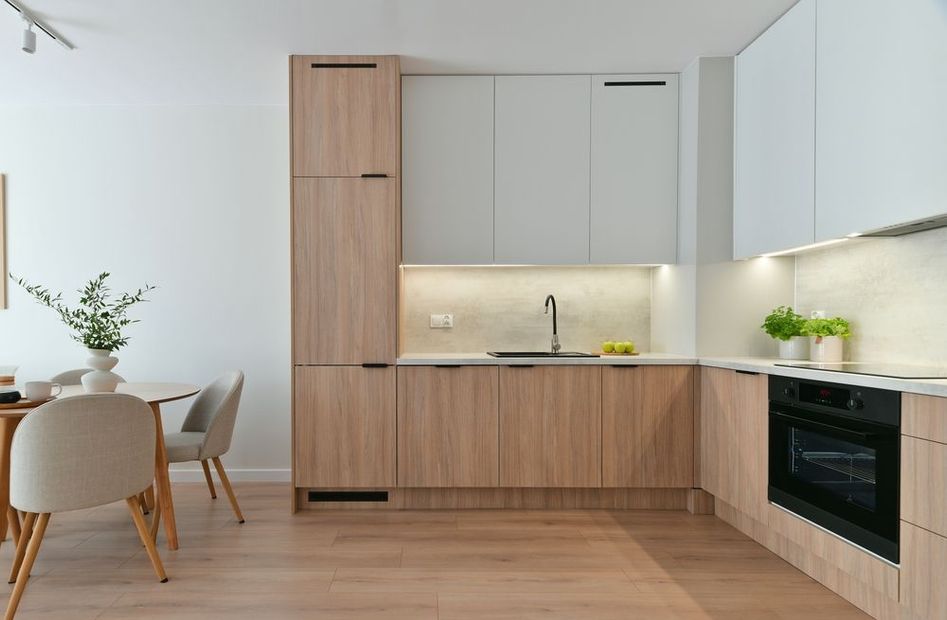 Cocina moderna y luminosa con armarios de madera clara, paredes blancas y una mesa de comedor junto a la ventana.