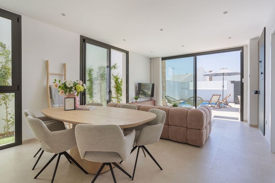 Salón-comedor moderno con mesa redonda, sillas beige, sofá y balcón con vistas al mar.