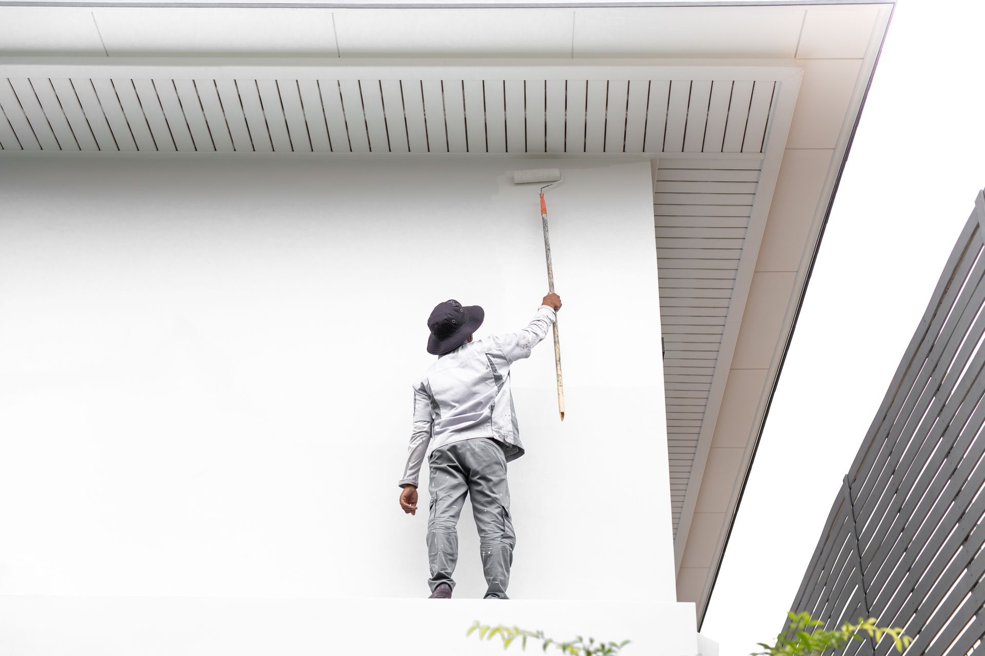 Une personne sur un échafaudage peint un mur extérieur blanc au rouleau.