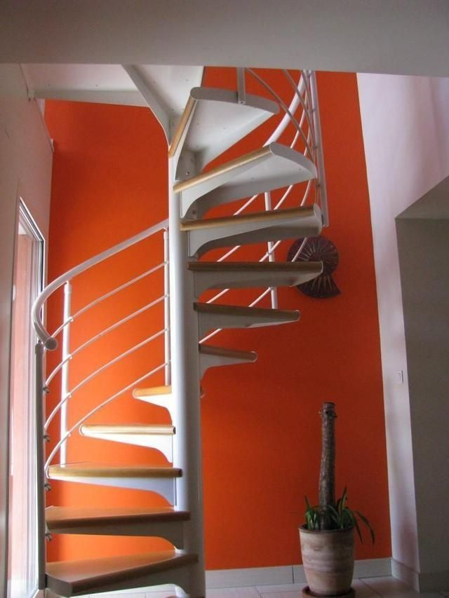 Escalier en colimaçon avec rampe blanche et mur orange.