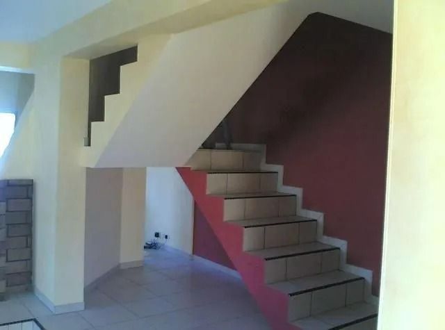 Escalier avec marches carrelées de couleur claire, panneaux latéraux rouges et murs blancs et beiges.