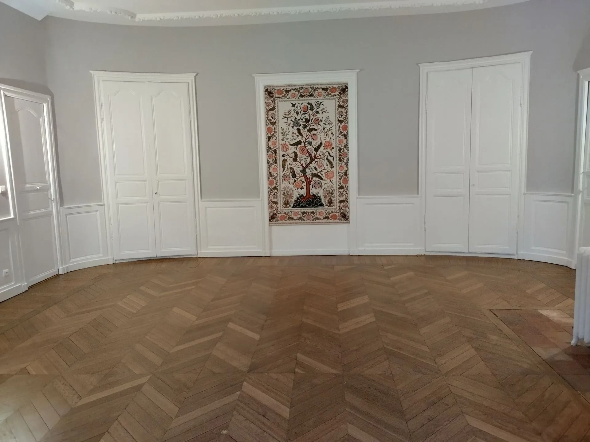 Pièce vide avec parquet, murs gris, portes blanches et une tapisserie.