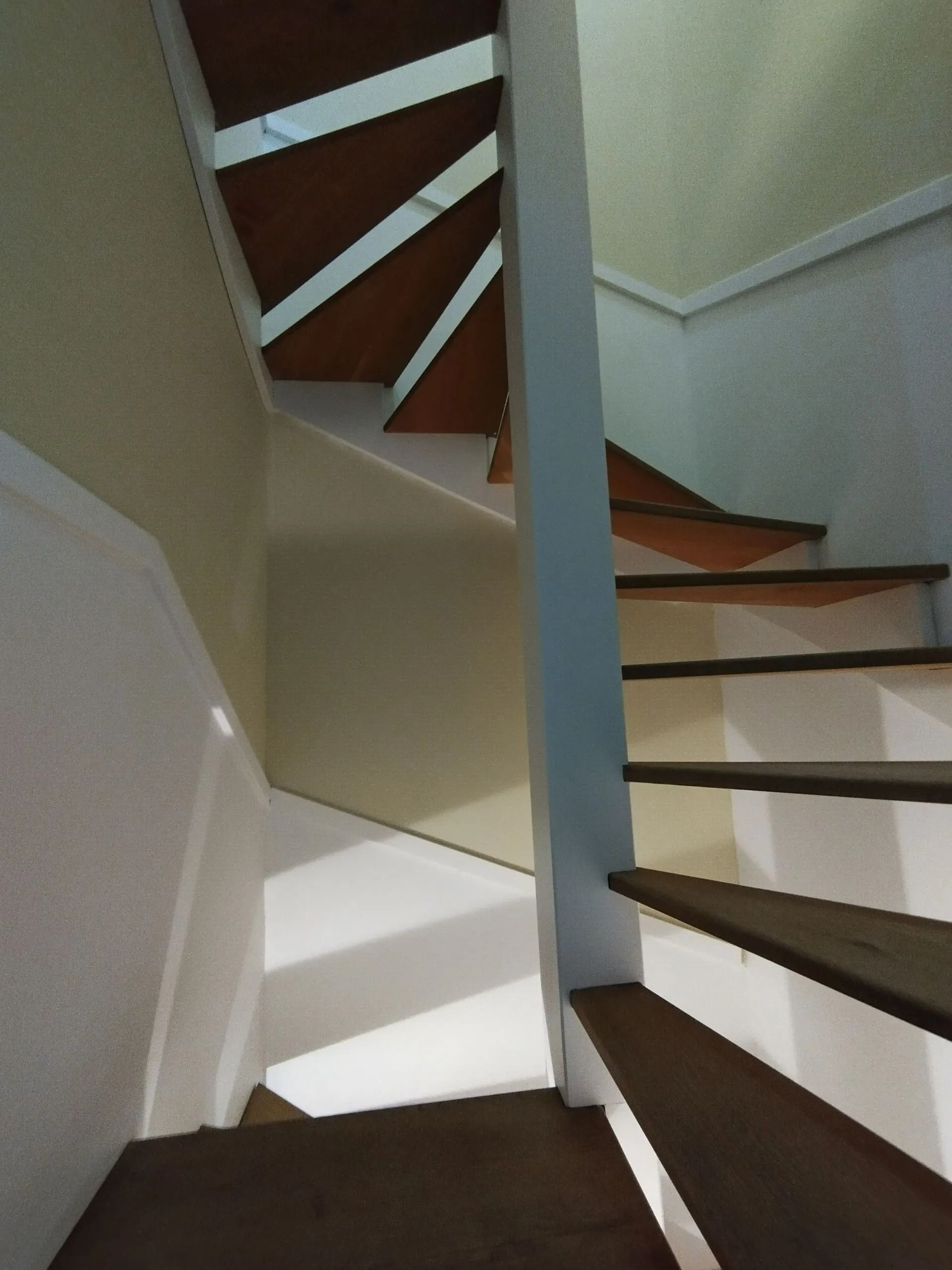 Escalier aux marches en bois et aux murs blancs, vu d'en bas, montant vers la lumière.