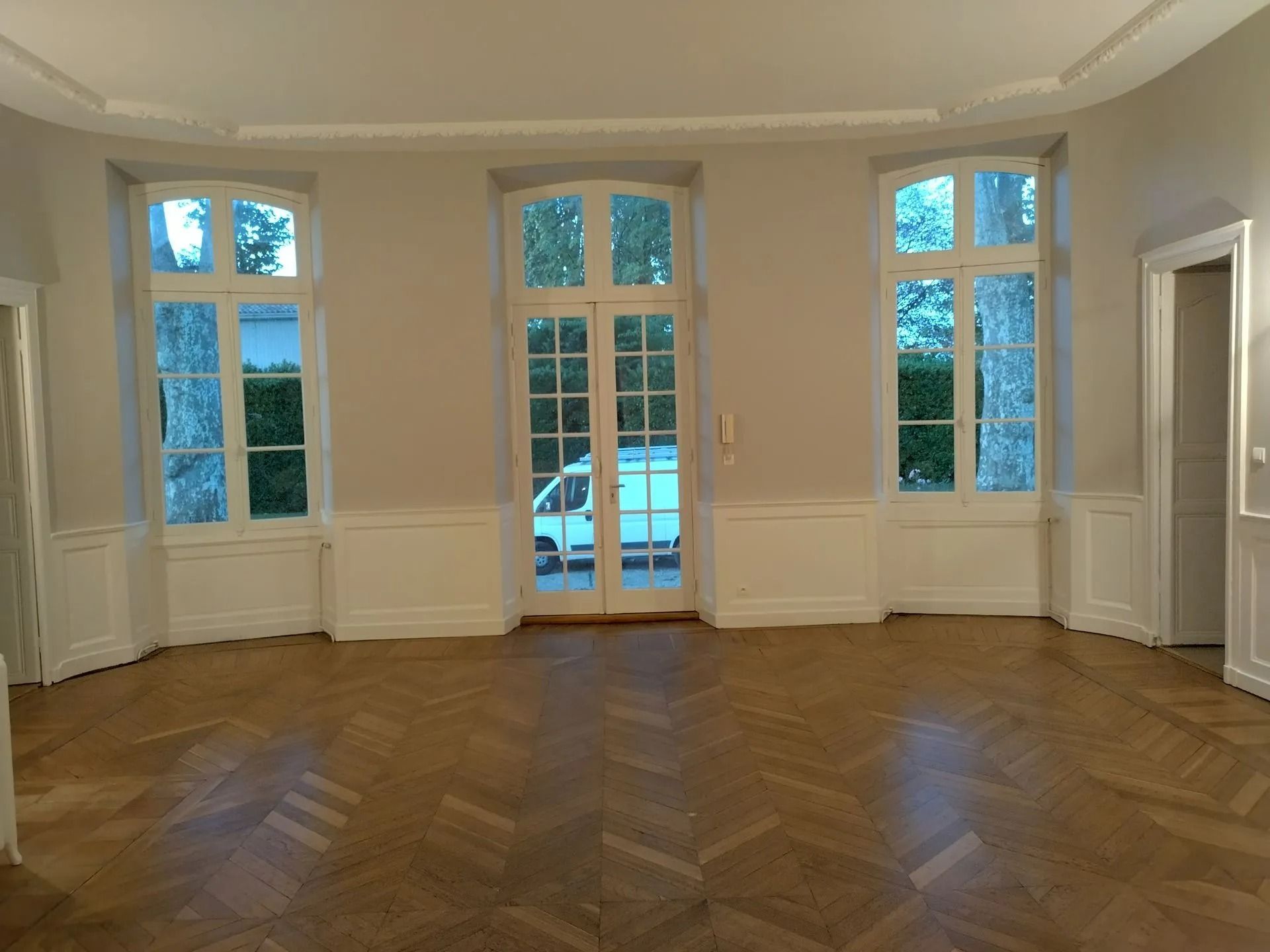 Intérieur de la pièce avec parquet, fenêtres à encadrement blanc et une porte donnant sur l'extérieur.