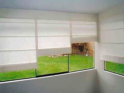 Una habitación con una gran ventana con persianas blancas y vista a un exuberante campo verde.