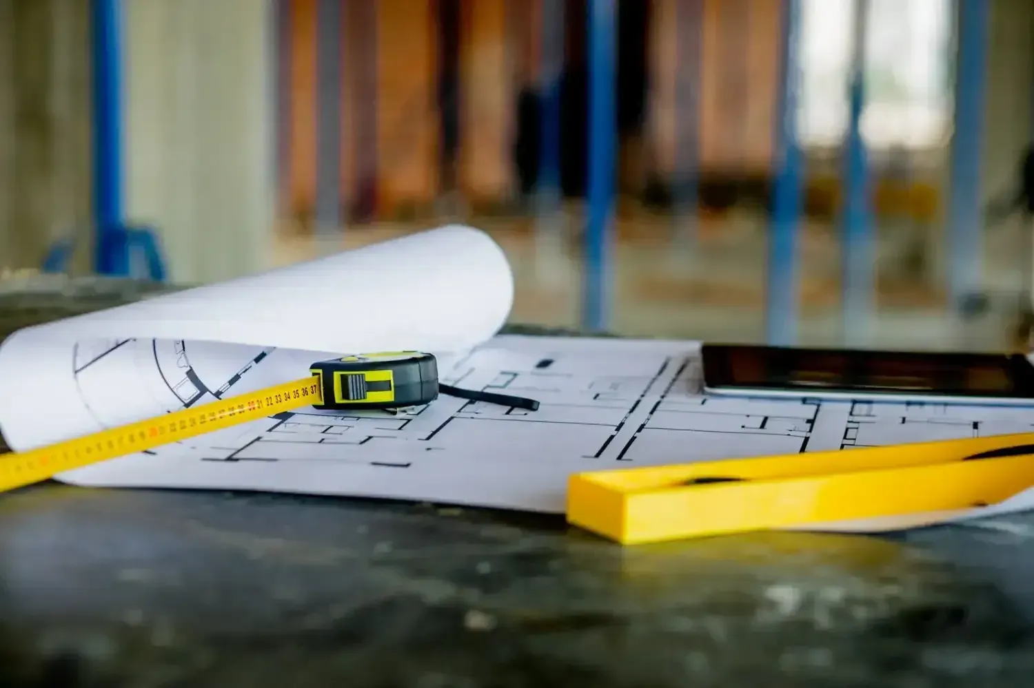 Plano enrollado con cinta métrica amarilla y lápiz sobre una mesa de construcción.