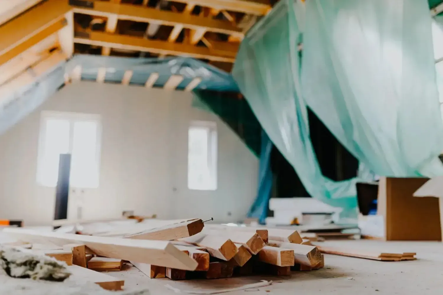 Obra en renovación con vigas de techo a la vista, láminas de plástico colgando y restos de madera en el suelo.