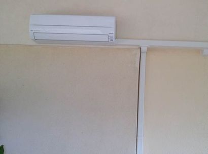 Climatiseur mural blanc au-dessus d'une cloison beige à l'intérieur.
