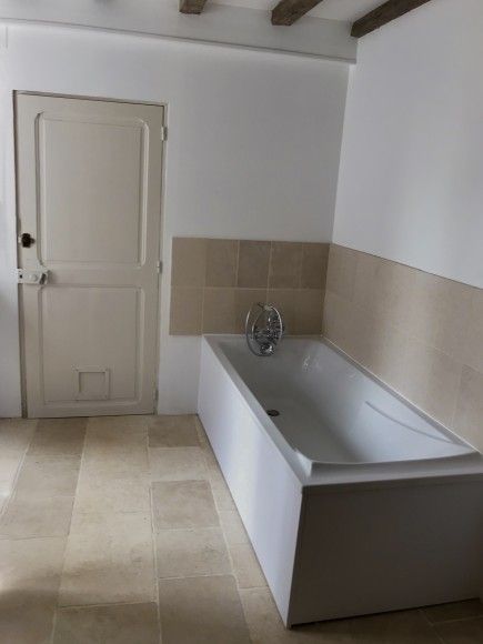 Salle de bains minimaliste avec carrelage beige, baignoire blanche et porte fermée.