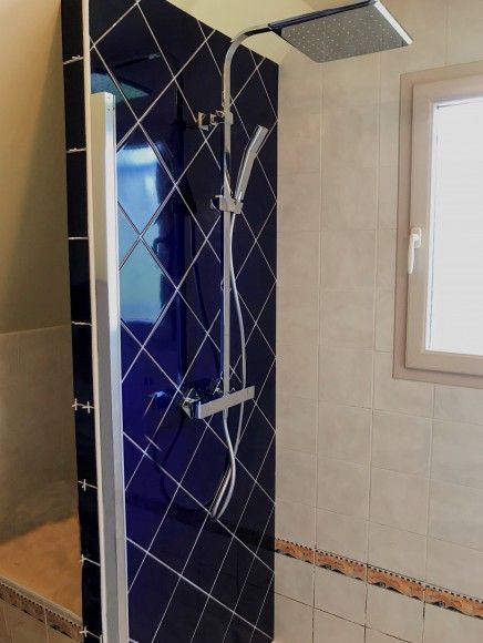Douche moderne avec carrelage bleu, robinetterie chromée et paroi de verre dans une salle de bains carrelée.