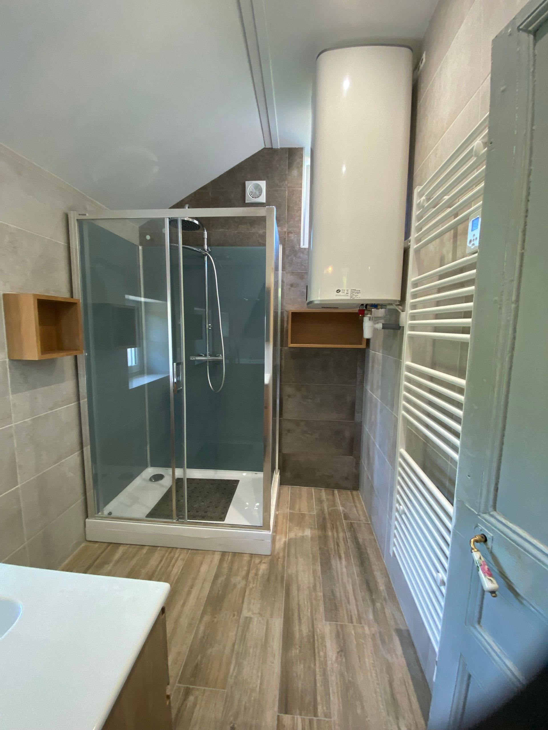 Salle de bains moderne avec douche en verre, sol imitation bois, sèche-serviettes blanc et chauffe-eau mural