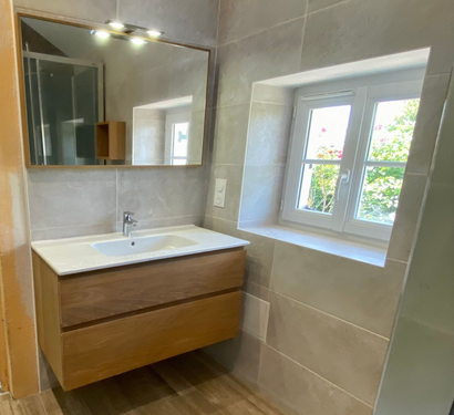 Meuble-lavabo moderne avec tiroirs en bois, lavabo blanc, miroir et petite fenêtre à côté.