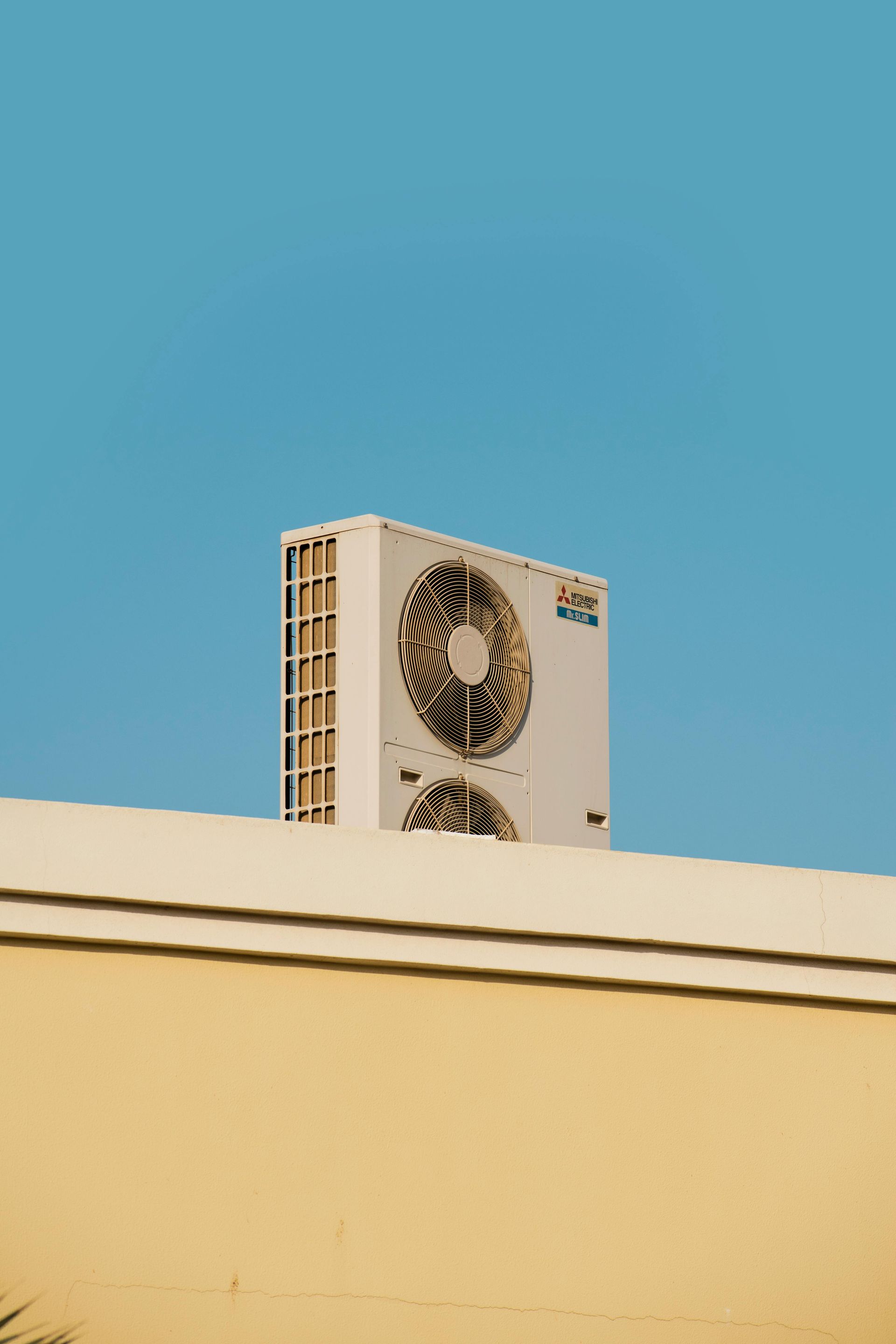 Unité de climatisation extérieure sur le toit d'un bâtiment beige, se détachant sur un ciel bleu.