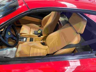 El interior de un Ferrari rojo con asientos de cuero color canela y un volante.
