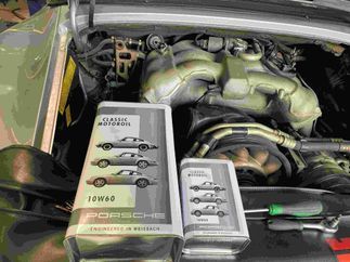 Una lata de aceite de motor Porsche está debajo del capó de un coche.
