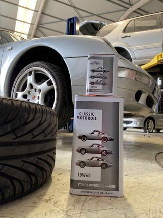 Una lata de aceite de motor Porsche está junto a un coche en un garaje.