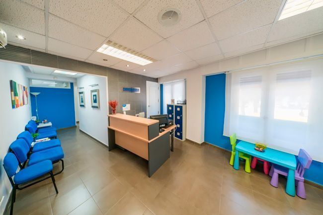 Una sala de espera con sillas azules y un escritorio.