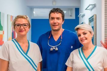 Un hombre y dos mujeres posan para una fotografía en un consultorio dental.