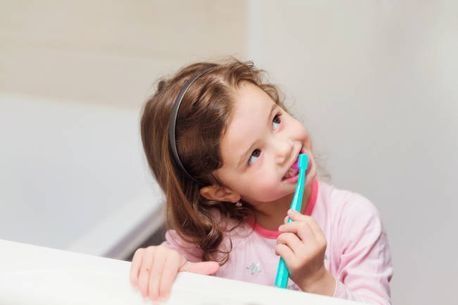 Una niña se cepilla los dientes frente a un espejo.