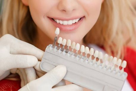 Una mujer sonríe mientras un dentista sostiene una tabla de colores de dientes.
