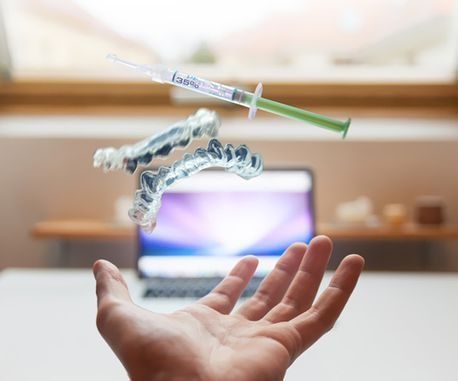 Una persona sostiene una bandeja dental y una jeringa en la mano frente a una computadora portátil.