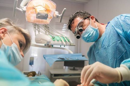 Un hombre y una mujer están operando a un paciente en un consultorio dental.