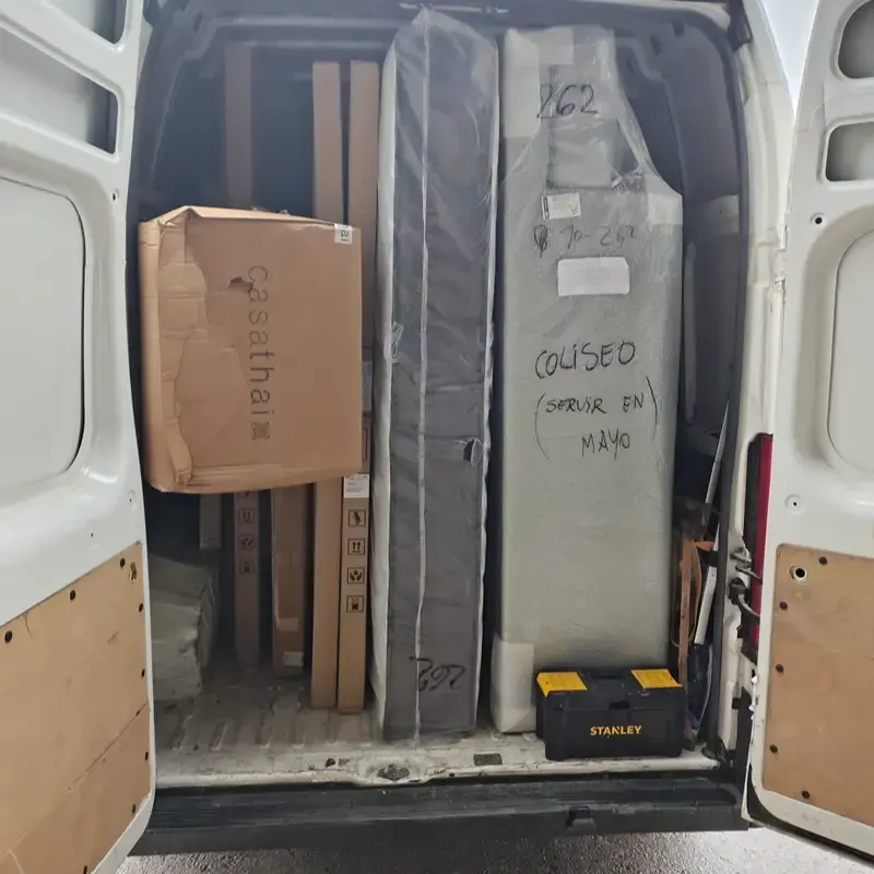 Furgoneta blanca de carga repleta de cajas de cartón y muebles envueltos dentro de las puertas traseras abiertas.