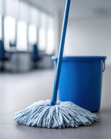 Une serpillière bleue et un seau assorti posés sur le sol dans un bureau dont la mise au point est floue.