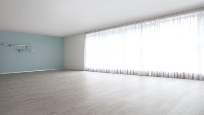 Una habitación vacía con una gran ventana y cortinas blancas.