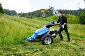 Ein Mann mäht mit einem Rasenmäher Gras auf einem Feld.