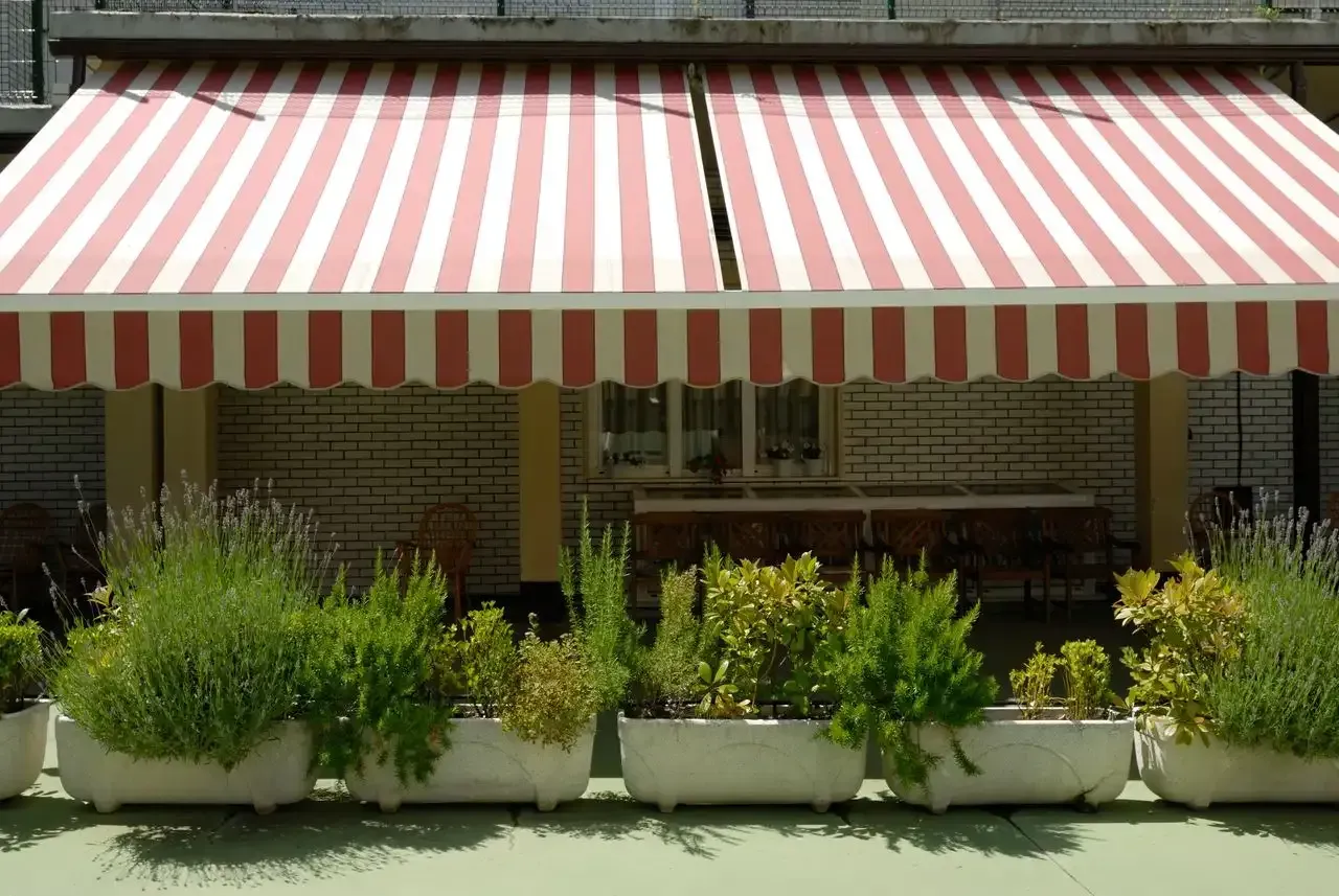 Un toldo de rayas rojas y blancas con jardineras debajo.