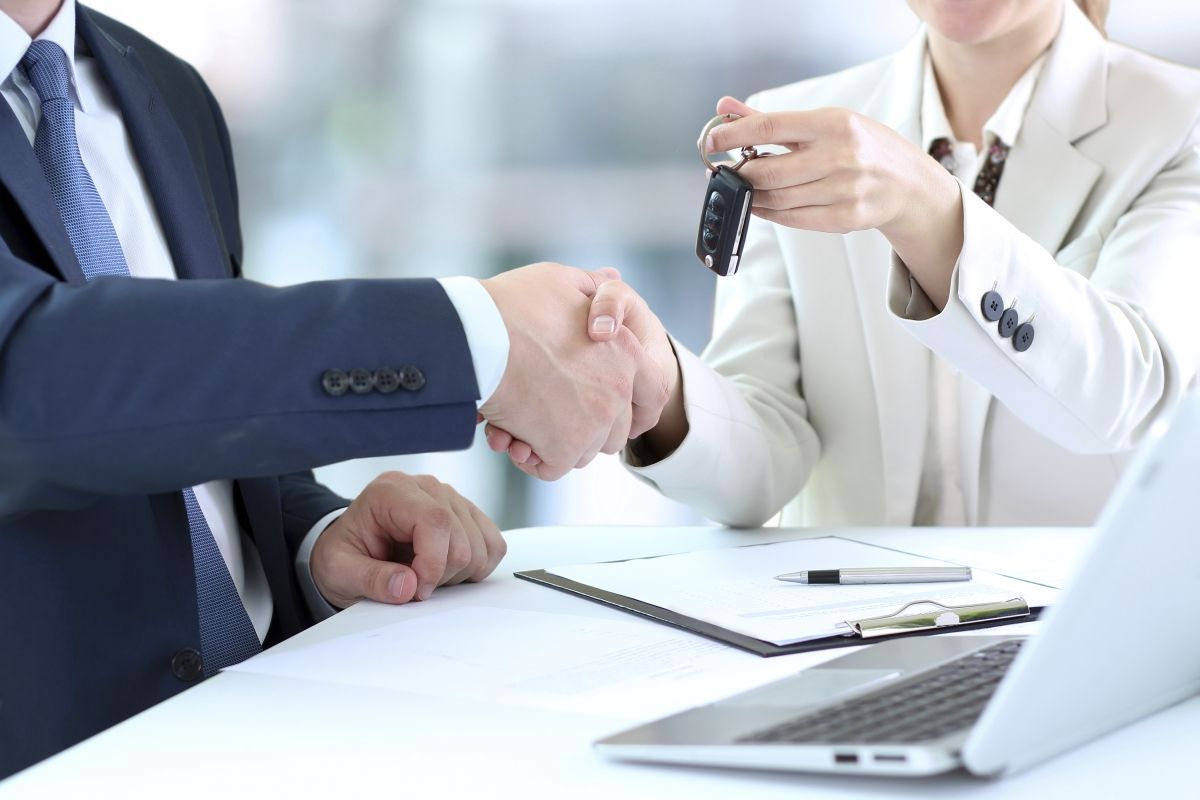 Un hombre y una mujer se dan la mano mientras una mujer sostiene una llave de coche.