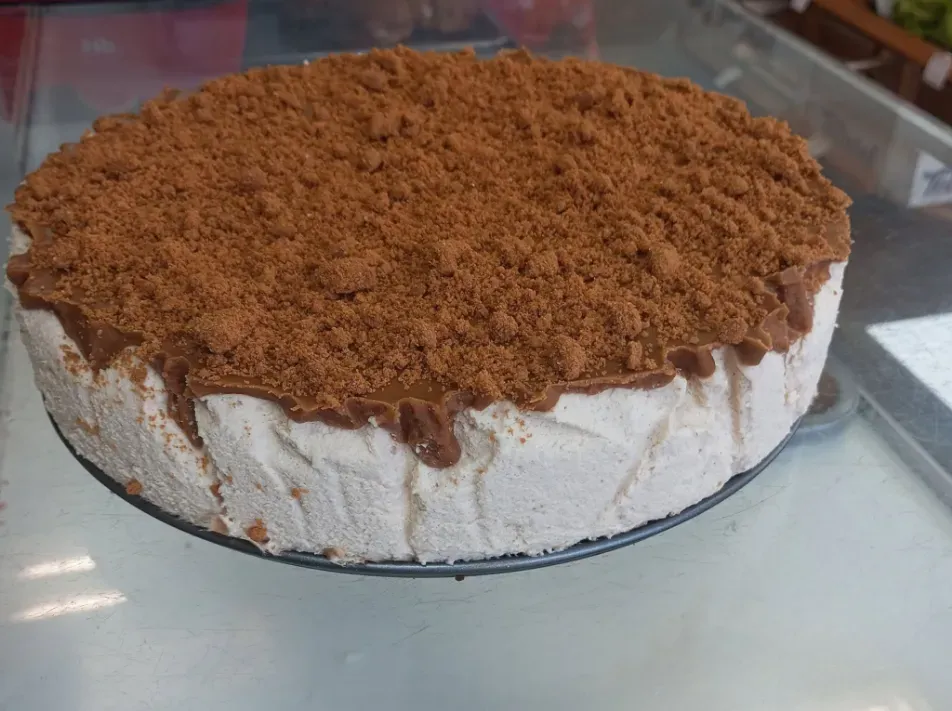 Pastel redondo cubierto con migas marrones desmenuzables sobre un soporte de vidrio.