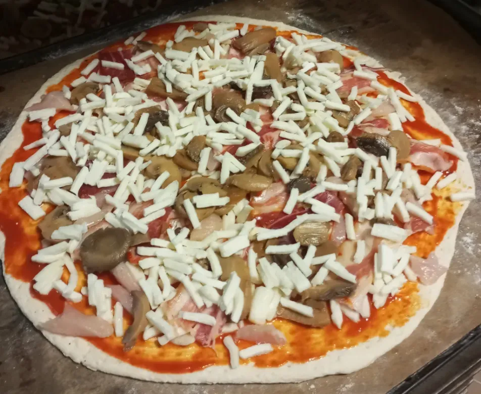 Pizza casera sin hornear cubierta con champiñones, queso y salsa de tomate en una bandeja para hornear.