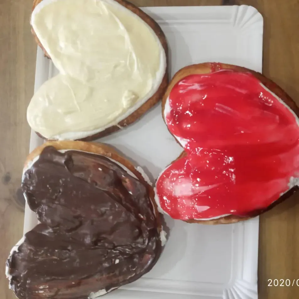 Tres galletas con forma de corazón con glaseado blanco, rojo y de chocolate sobre un plato blanco.