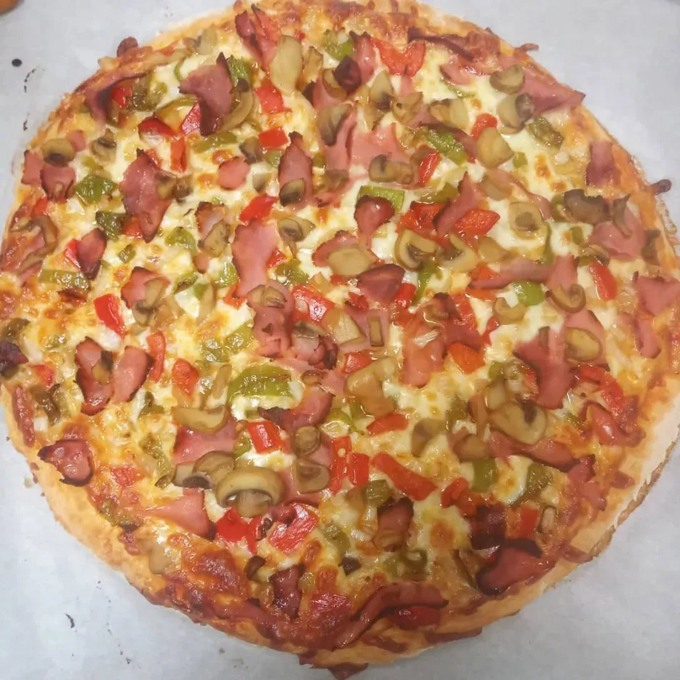 Pizza redonda casera cubierta con pepperoni, pimientos verdes, champiñones y queso fundido sobre papel pergamino.