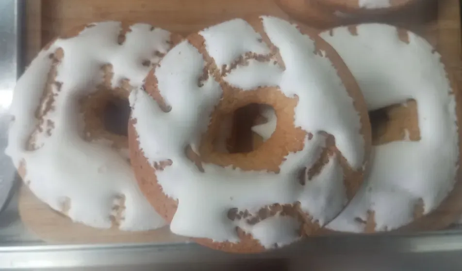 Bandeja de rosquillas con glaseado blanco y bizcocho marrón que se asoma entre el glaseado.