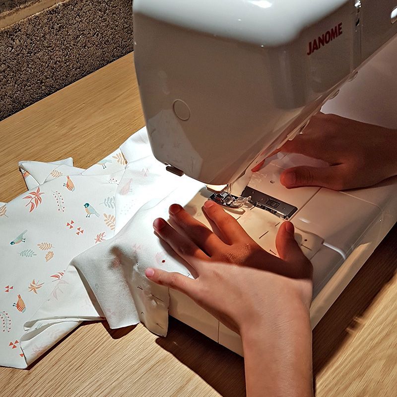 Des mains cousent du tissu avec une machine à coudre Janome sur une surface en bois.