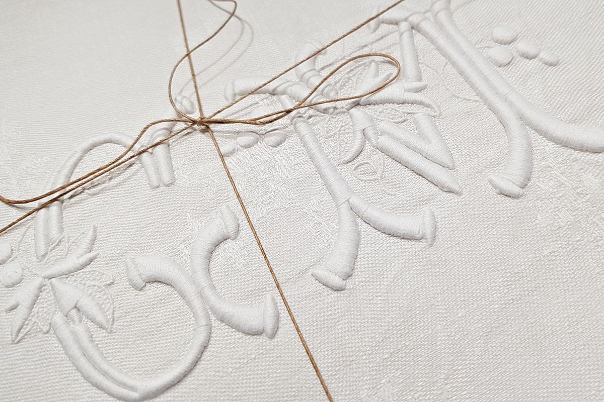 Tissu blanc à motif floral en relief, noué avec de la ficelle marron.