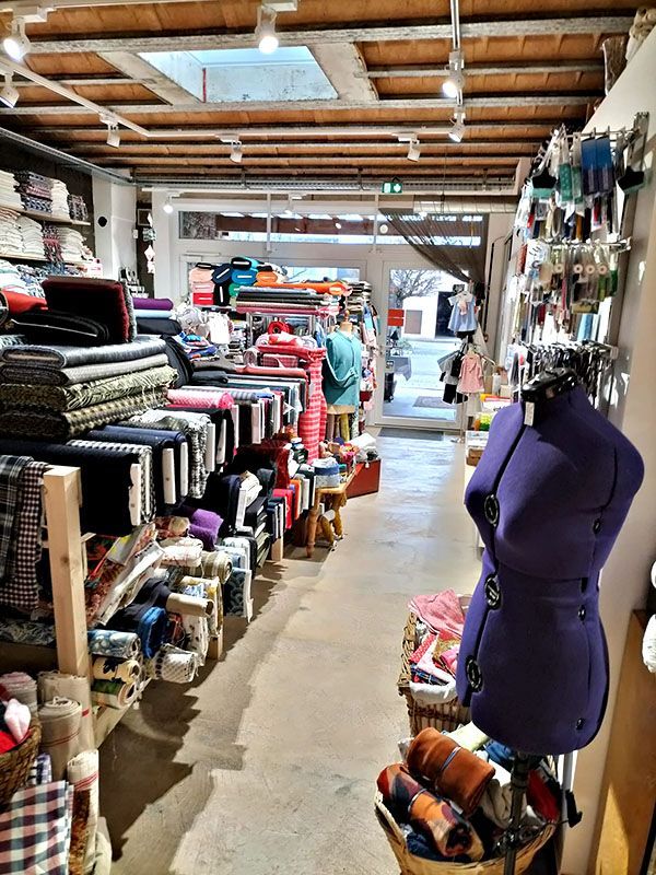 Intérieur d'un magasin de tissus avec des rouleaux de tissu sur des étagères et un mannequin.