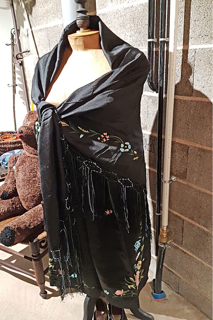 Châle noir à franges et broderies florales drapé sur un mannequin.