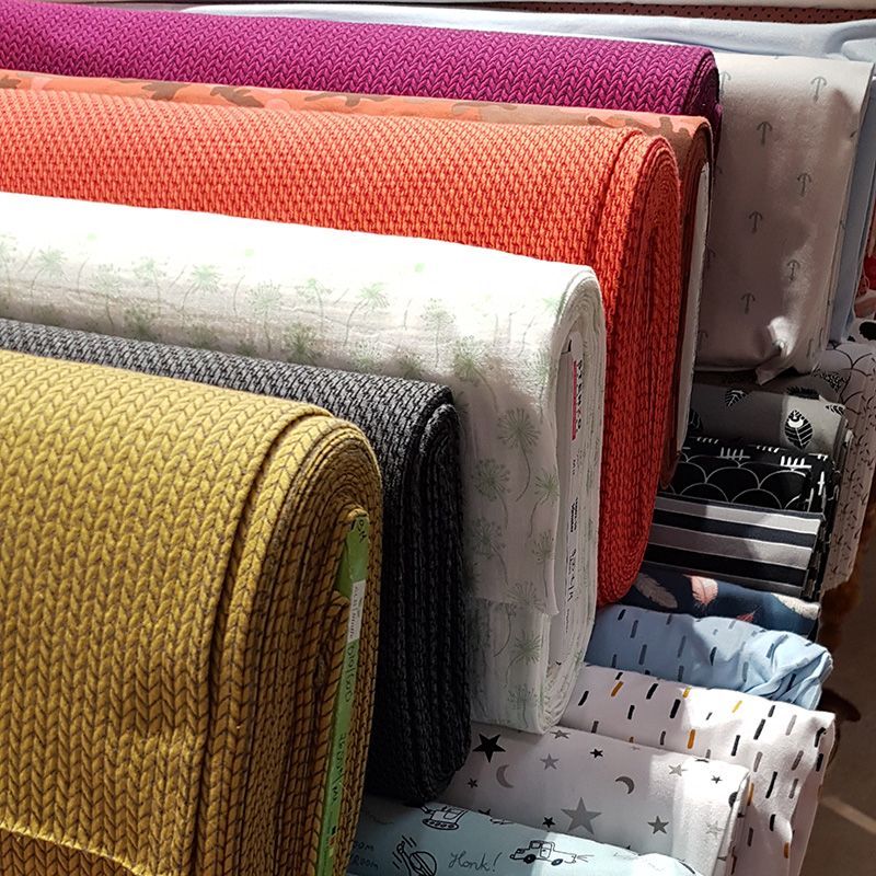 Gros plan sur des rouleaux de tissu de couleurs et de motifs variés, notamment orange, jaune et bleu.