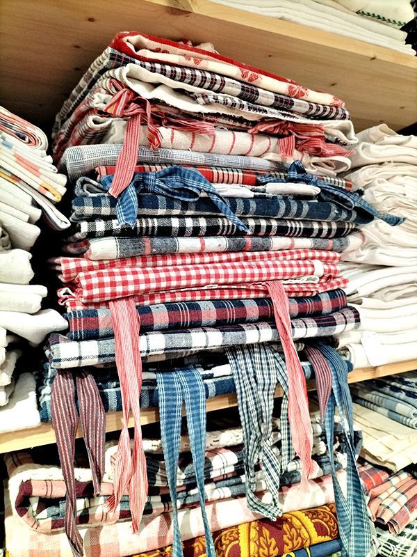 Pile de tissus à carreaux et à rayures pliés et attachés par des rubans sur une étagère en bois.