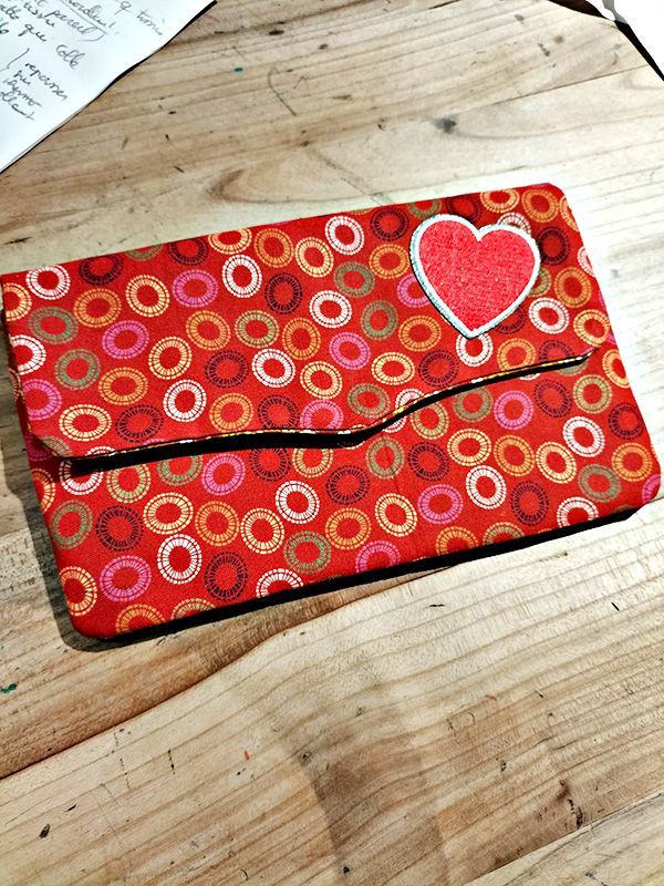 Pochette en tissu rouge ornée d'un appliqué en forme de cœur, posée sur une table en bois.