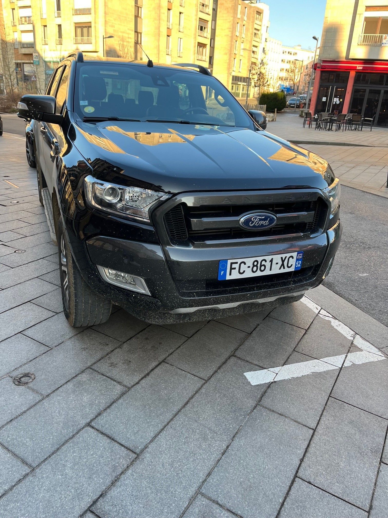 Un pick-up Ford Ranger noir, immatriculé en France, est garé sur des pavés.