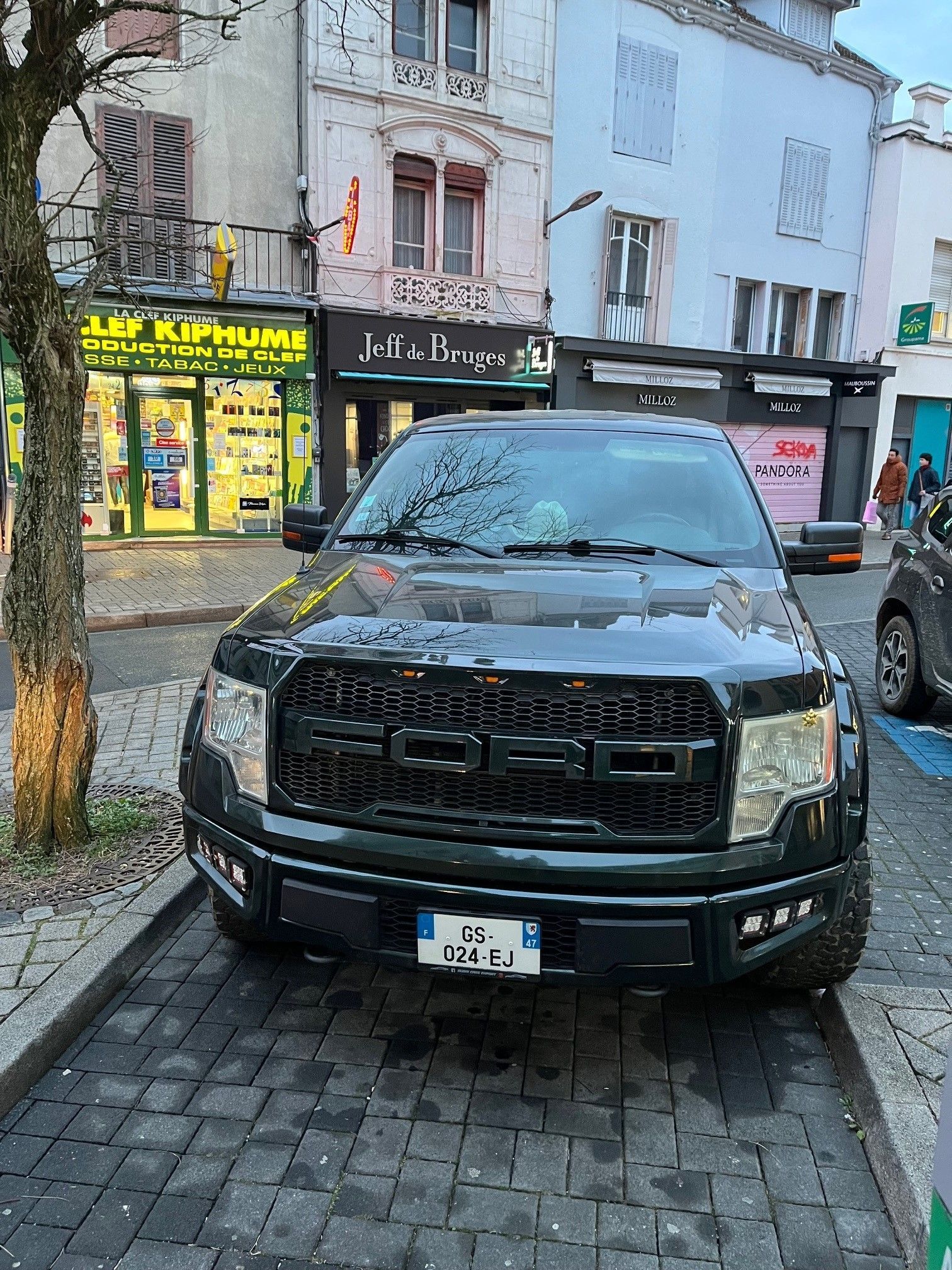 Camion Ford noir stationné dans une rue pavée, devantures de magasins en arrière-plan.